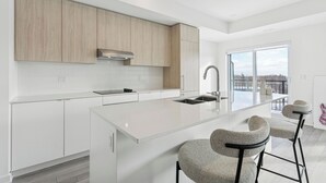 A modern kitchen with white cabinetry, a large island, and bar stools. - Home Richmond Hill 2bed2.5bath | Parking (Richmond Hill)
