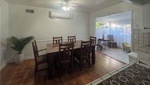 Een eethoek met een houten tafel en stoelen, een plafondventilator en uitzicht op buiten door een deur.
