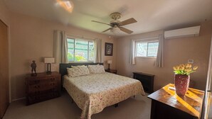 Een slaapkamer met een bed, een dressoir, nachtkastjes, een plafondventilator, ramen en een vaas met bloemen.