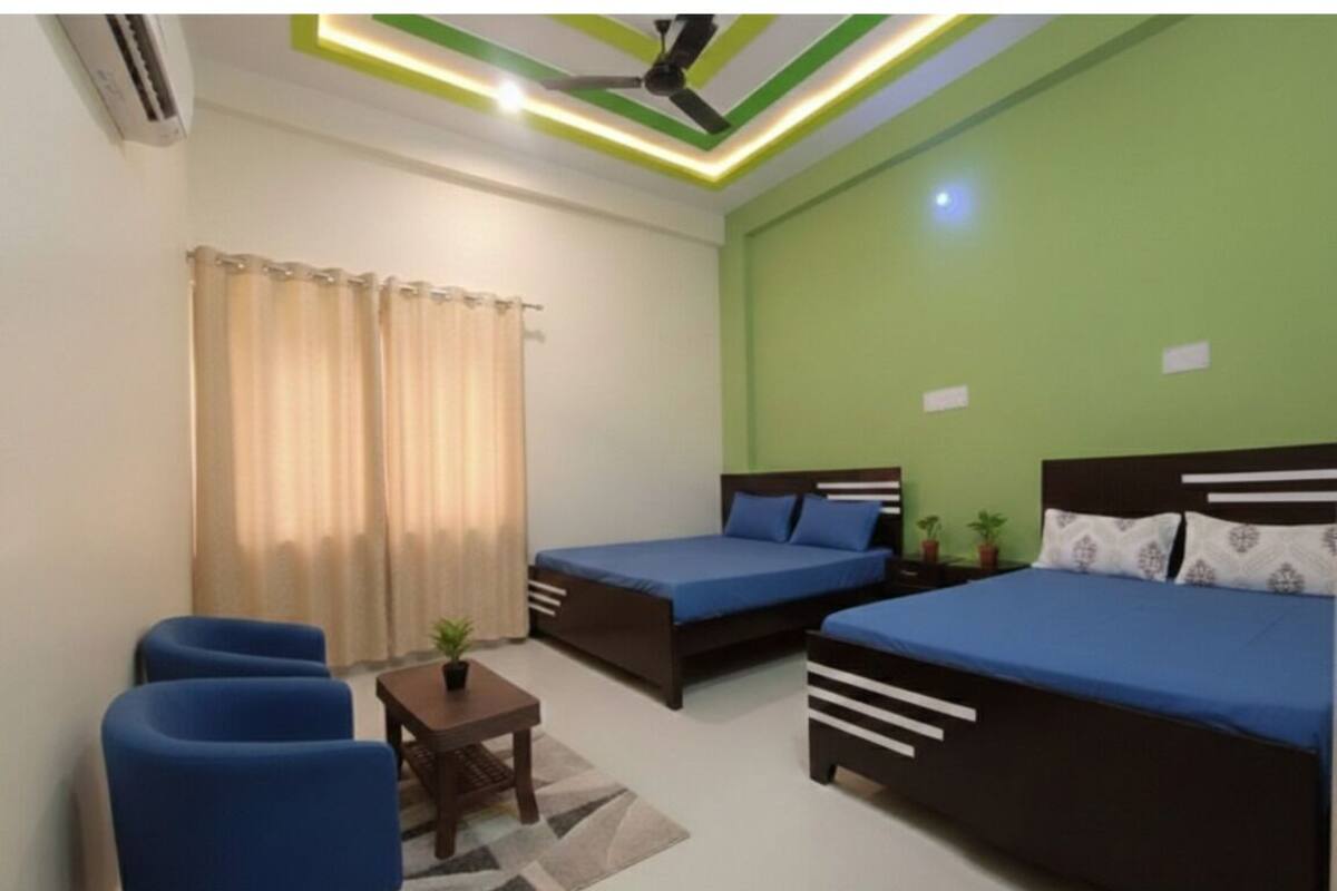 A room with two beds, a small table, two chairs, and a ceiling fan.