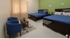 Un dormitorio con dos camas, una mesita, una silla y un ventilador de techo.