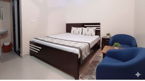 Un dormitorio con cama, mesita de noche, silla y una pequeña mesa con una planta.