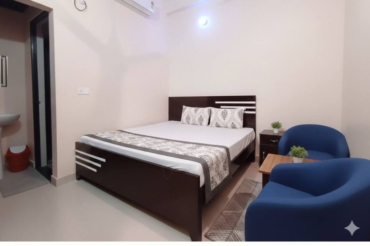 A bedroom with a bed, bedside table, chair, and a small table with a plant.