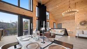 Een ruim houten interieur met een eethoek, een gezellige zithoek en grote ramen met uitzicht op de omgeving.