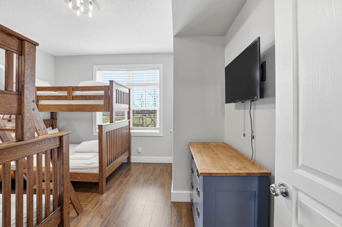 A bedroom with bunk beds, a TV mounted on the wall, and a wooden desk.