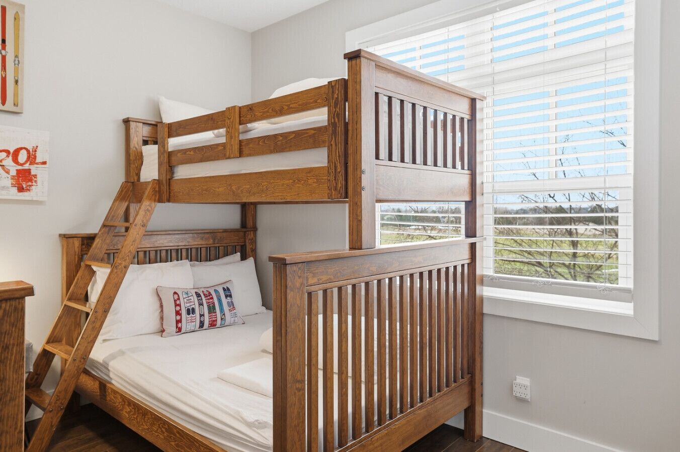 A bunk bed with a wooden frame, white bedding, and a view of a green landscape through the window.