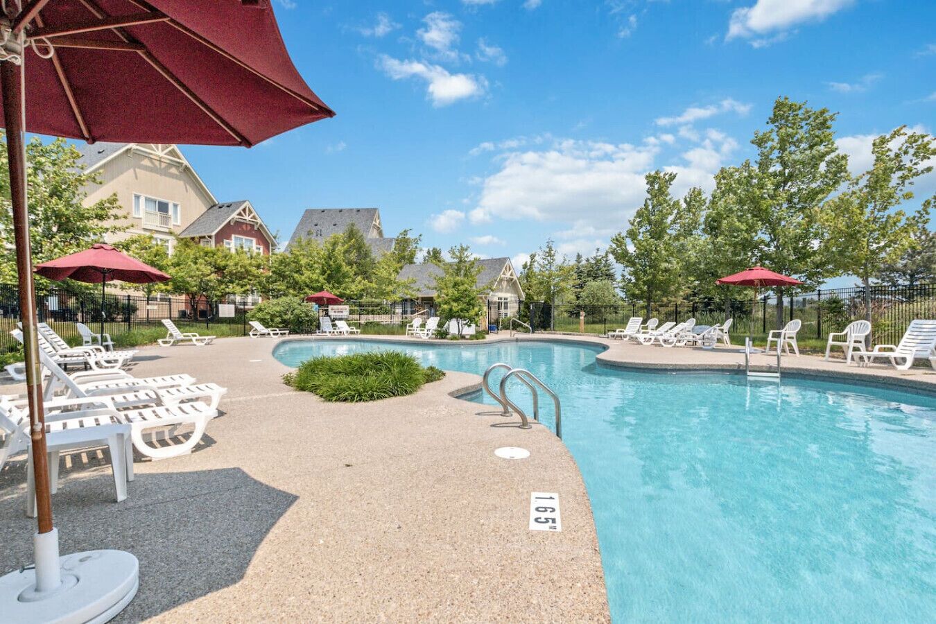 A swimming pool with lounge chairs and umbrellas, surrounded by trees and houses.