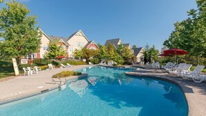 Ein klares Schwimmbecken mit Liegestühlen und Sonnenschirmen, umgeben von Bäumen und Gebäuden.