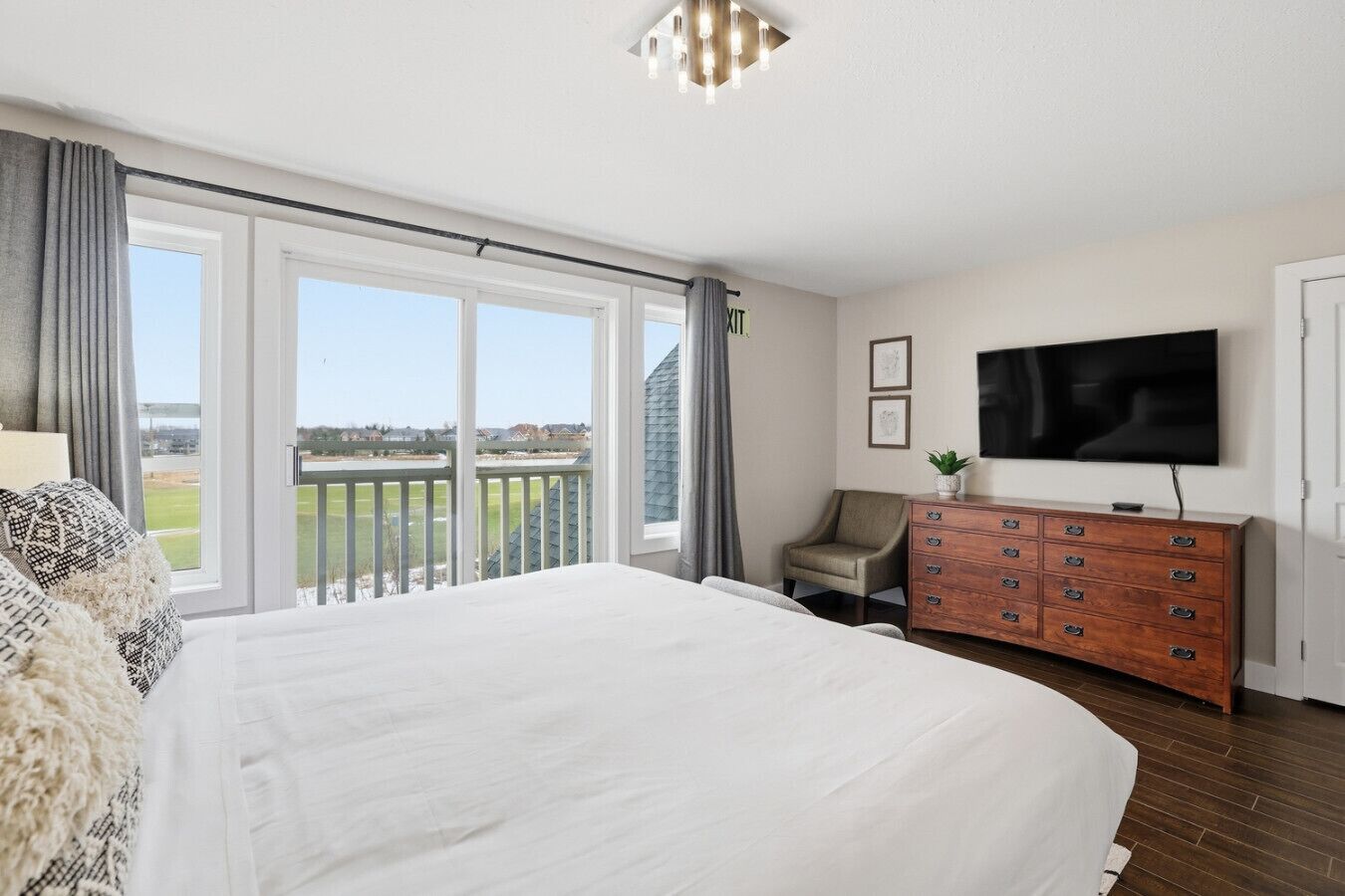 Une chambre avec un grand lit, une commode, une télévision et un balcon donnant sur l’extérieur.