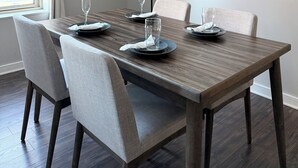 A dining area with a wooden table set for four, chairs, a floor lamp, and a painting on the wall.