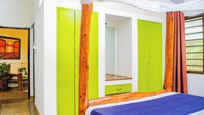 Ein Zimmer mit einem Bett, einem grünen Kleiderschrank, einem Spiegel und einem Fenster mit Vorhängen.
