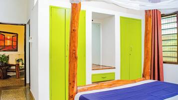Une pièce avec un lit, une armoire verte, un miroir et une fenêtre avec des rideaux.