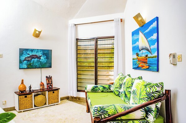 A room with a bed, a TV, a window with curtains, and artwork on the walls.