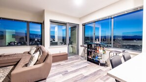 Ein modernes Wohnzimmer mit einer Couch, einer Bar mit Flaschen und großen Fenstern mit Blick auf die Stadt.