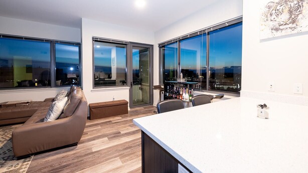 Ein modernes Wohnzimmer mit einer Couch, einem Essbereich mit Bar, großen Fenstern und Blick auf die Stadt.