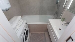 Une salle de bain compacte équipée d’un lave-linge, d’une baignoire et d’une douche.