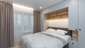 Une chambre à coucher moderne avec un lit, des rideaux, une table de chevet et des étagères intégrées.