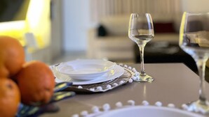 Ein Esstisch mit einem Teller, einem Glas und einem Glas Wasser. Auf dem Tisch liegen Orangen.