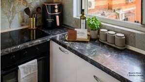 Eine moderne Küche mit Marmorarbeitsplatten, einer Montrix-Kaffeemaschine und Blick auf ein rot backsteins Gebäude durch das Fenster.