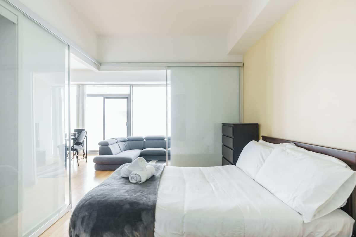 Um quarto moderno com cama, um sofá escuro, uma mesinha e um guarda-roupa.