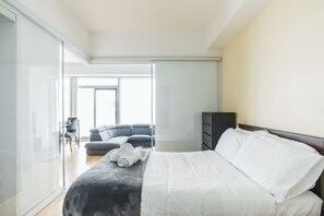 Un dormitori modern amb un llit, un sofà de color fosc, una taula petita i un armari.