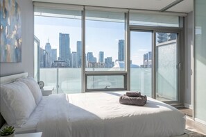 A bedroom with a large bed, a city view through floor-to-ceiling windows, and a modern design.