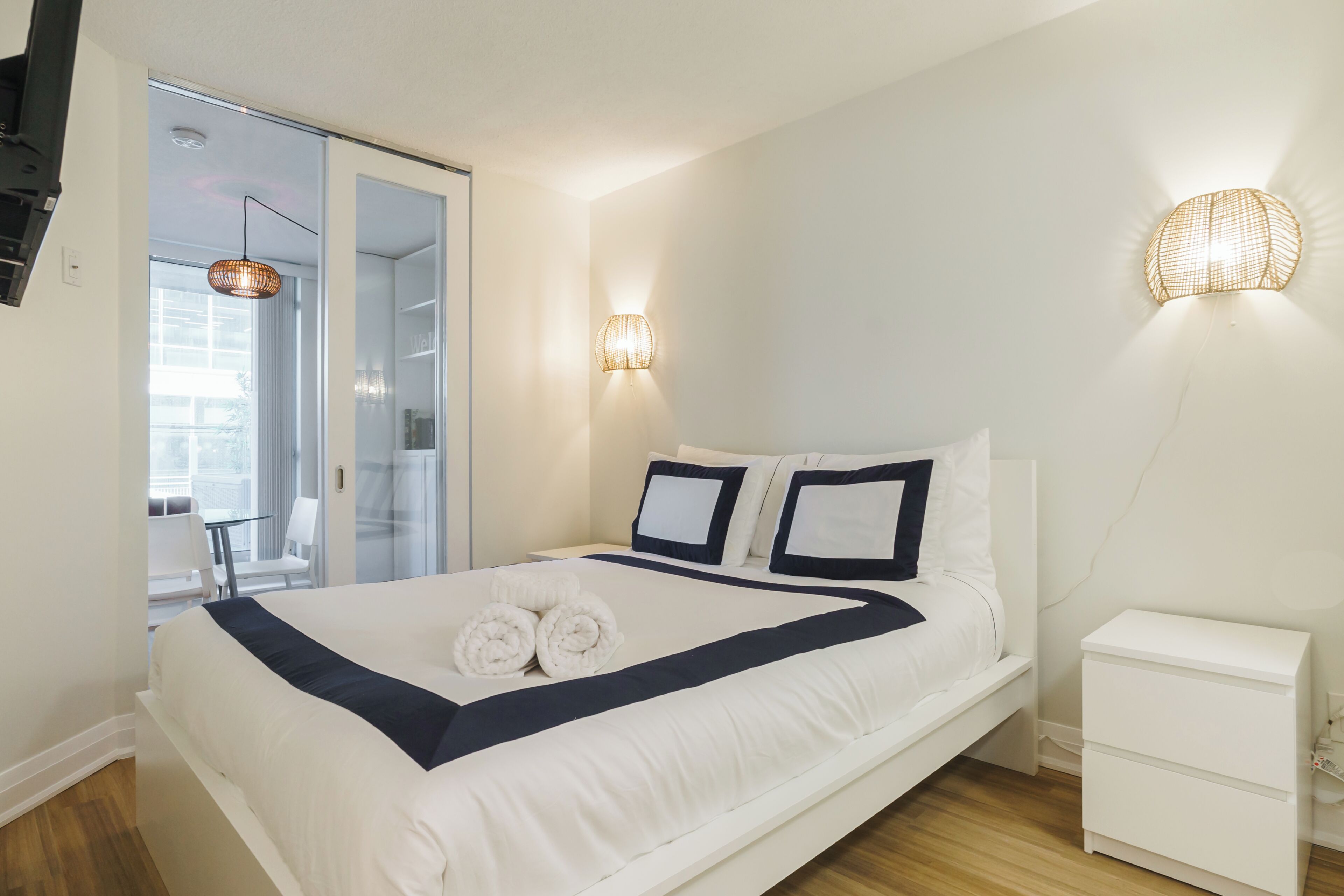 Une chambre d’hôtel moderne, dotée d’un grand lit, d’une table de chevet, d’une lampe fixée au mur et offrant une vue sur l’extérieur.
