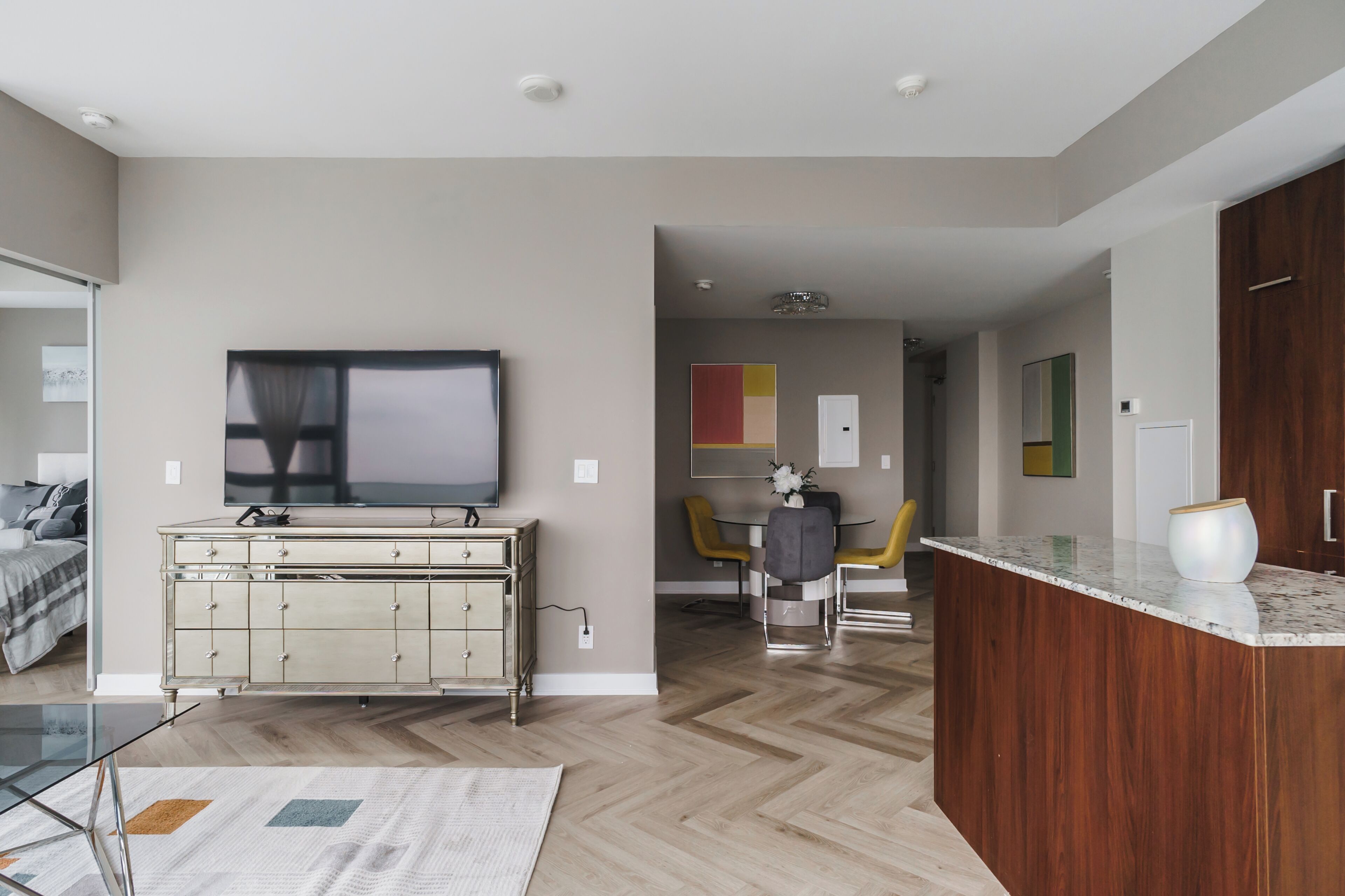 A modern living room with a TV, a wooden cabinet, and a dining area with yellow chairs.