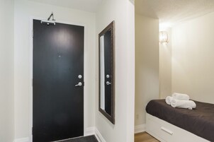 Een kamer met een zwarte deur, een grote spiegel, een bed met een bruine plaid en een wandlamp.