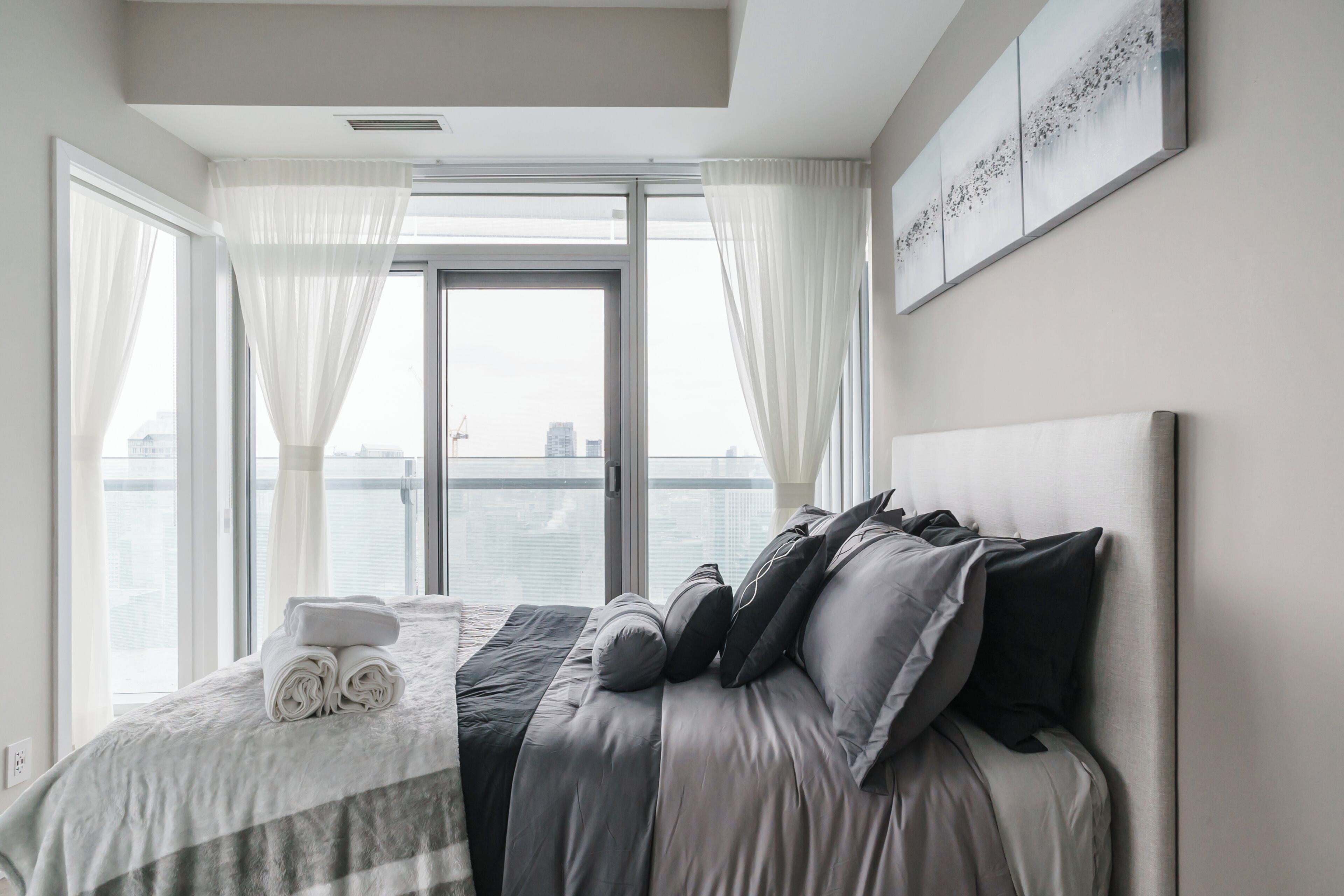A modern hotel room with a large bed, a view of the city through floor-to-ceiling windows, and a balcony.