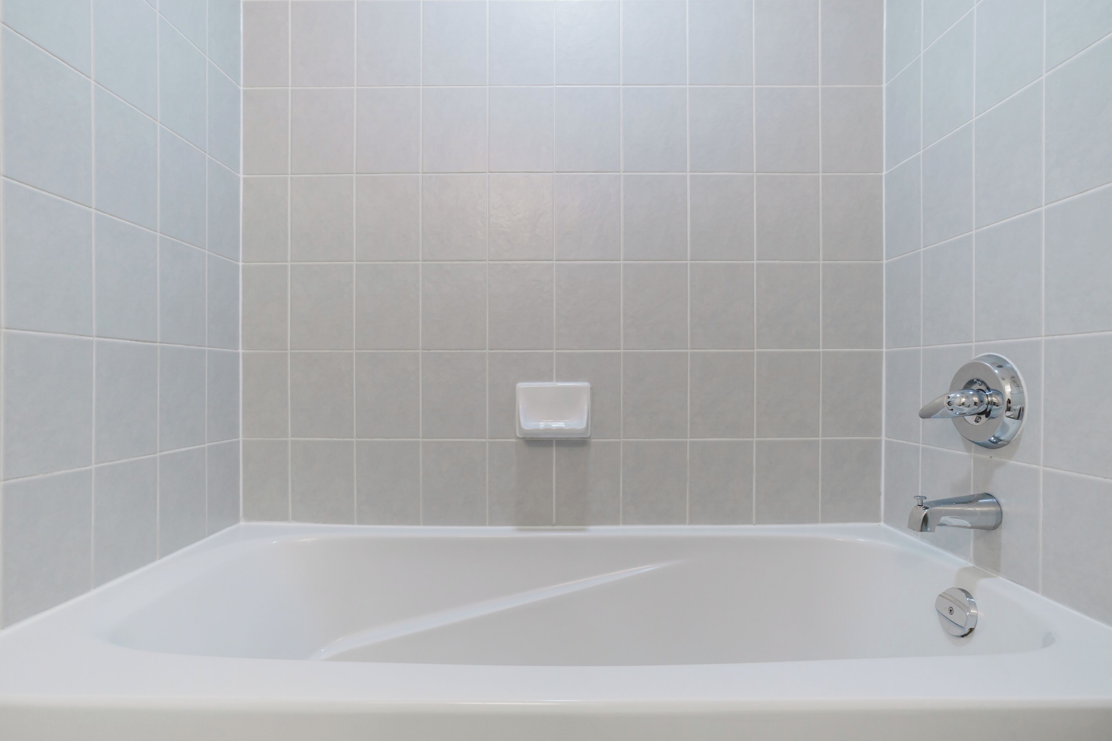 A modern bathroom with a white bathtub, tiled walls, and a chrome faucet.