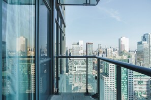 A high-rise building with a glass facade and a metal railing, offering a view of a cityscape with various buildings.