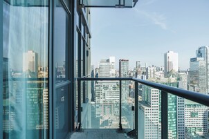 Een hoog gebouw met een glazen gevel en een metalen hekwerk, met uitzicht op een stadsgezicht met diverse gebouwen.