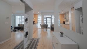 A modern kitchen with a dining area, a washing machine, and a large window providing natural light.