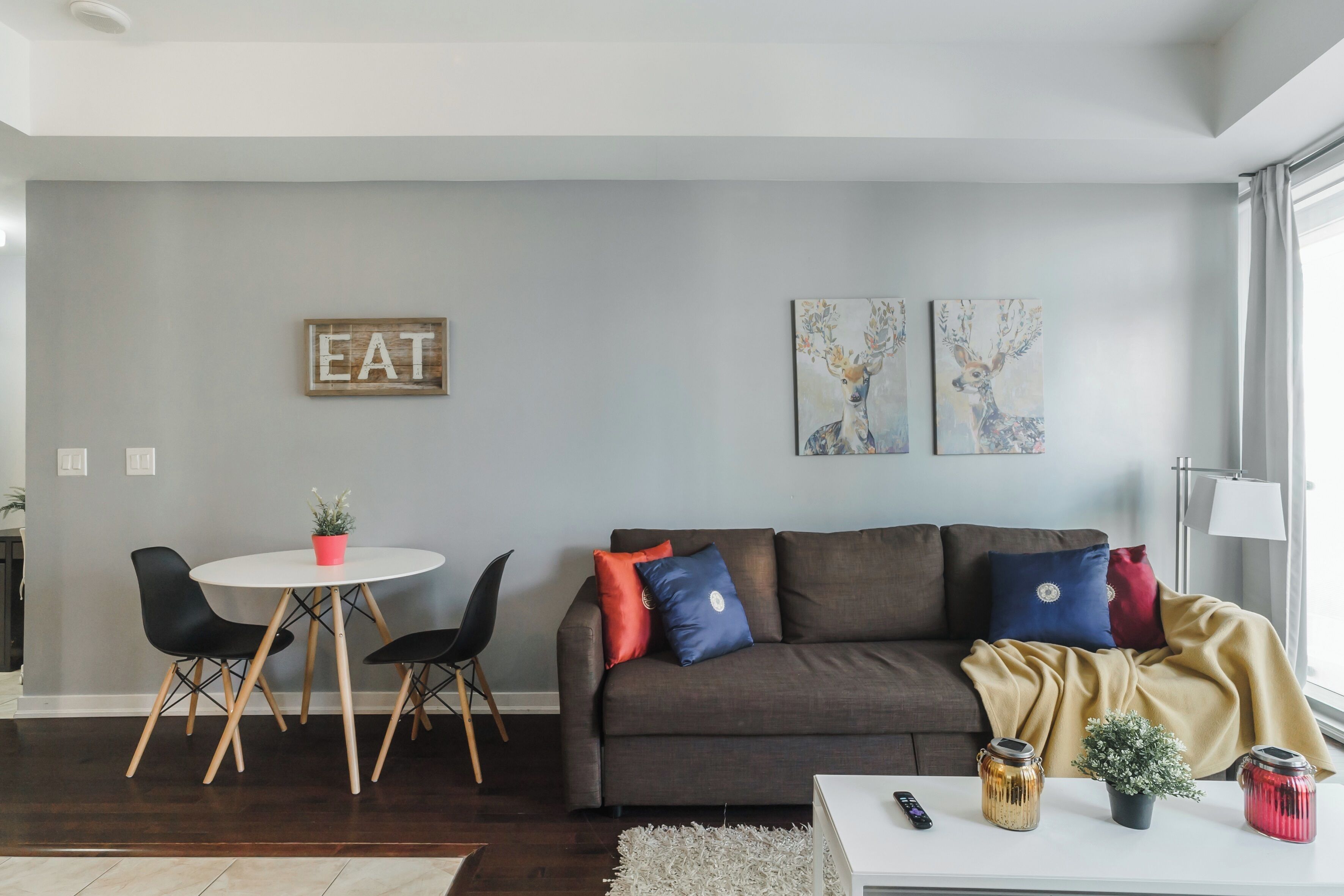 Un salon moderne avec un canapé gris, une table à manger avec des chaises et deux tableaux accrochés au mur.