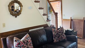 Ein Wohnzimmer mit einem braunen Ledersofa, zwei gemusterten Zierkissen, einem Holztisch und einer Treppe mit Holzhandläufen.