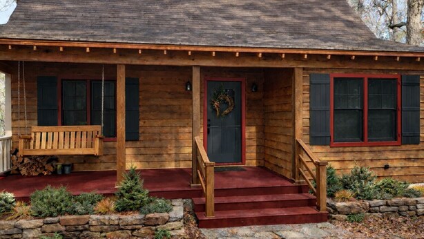Eine Holzhütte mit Veranda, einer Eingangstür mit Kranz und Stufen zum Eingang.