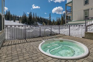 A hot tub on a paved patio with a view of a snowy mountain landscape and a building in the background. - Cozy top floor fully-equipped Creekside studio condo w/views, ski-in/out (Vernon)
