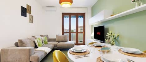 A modern living room with a sofa, dining table set for four, and a television.