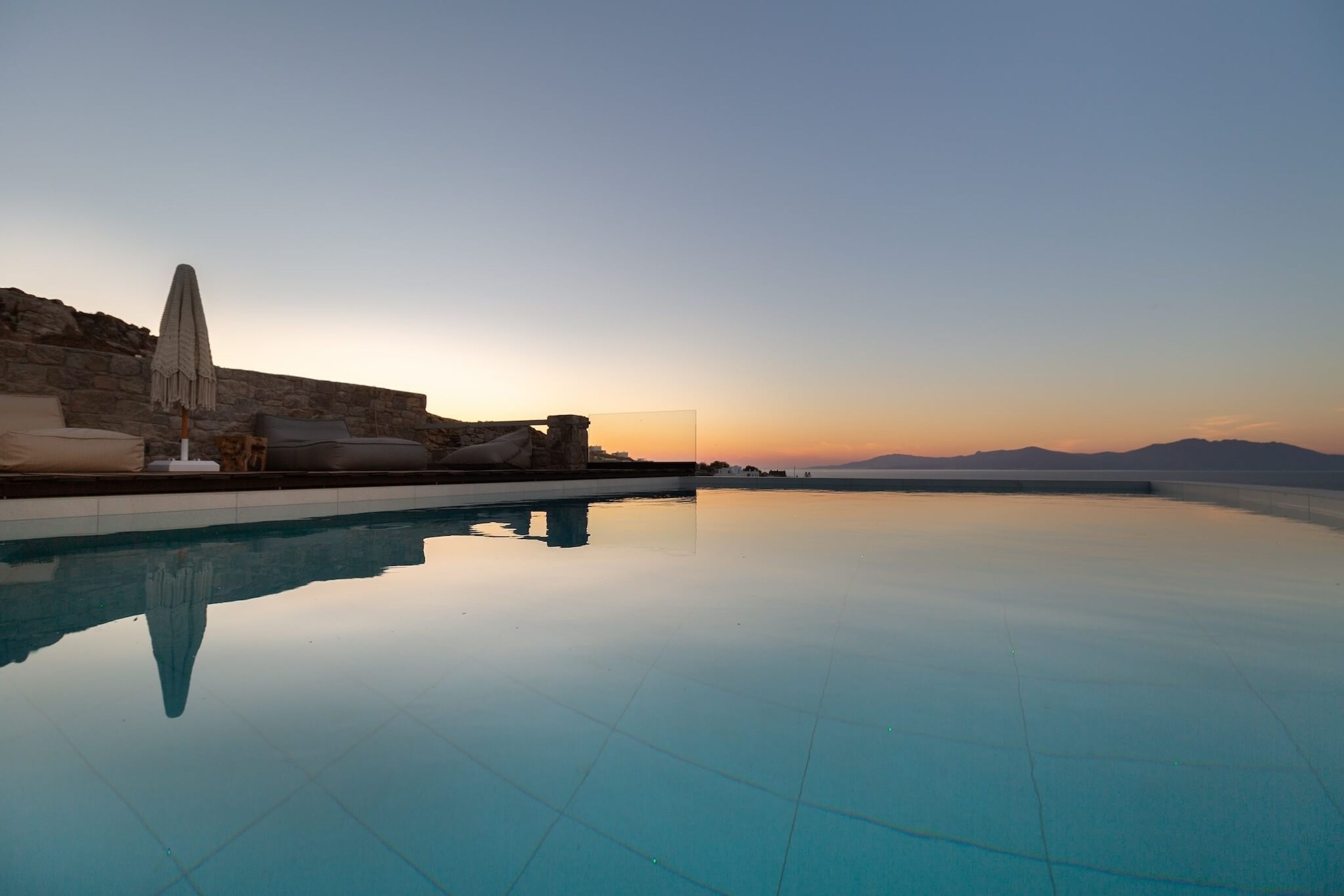 Une piscine à débordement paisible, offrant une vue dégagée sur le coucher du soleil et les montagnes lointaines.
