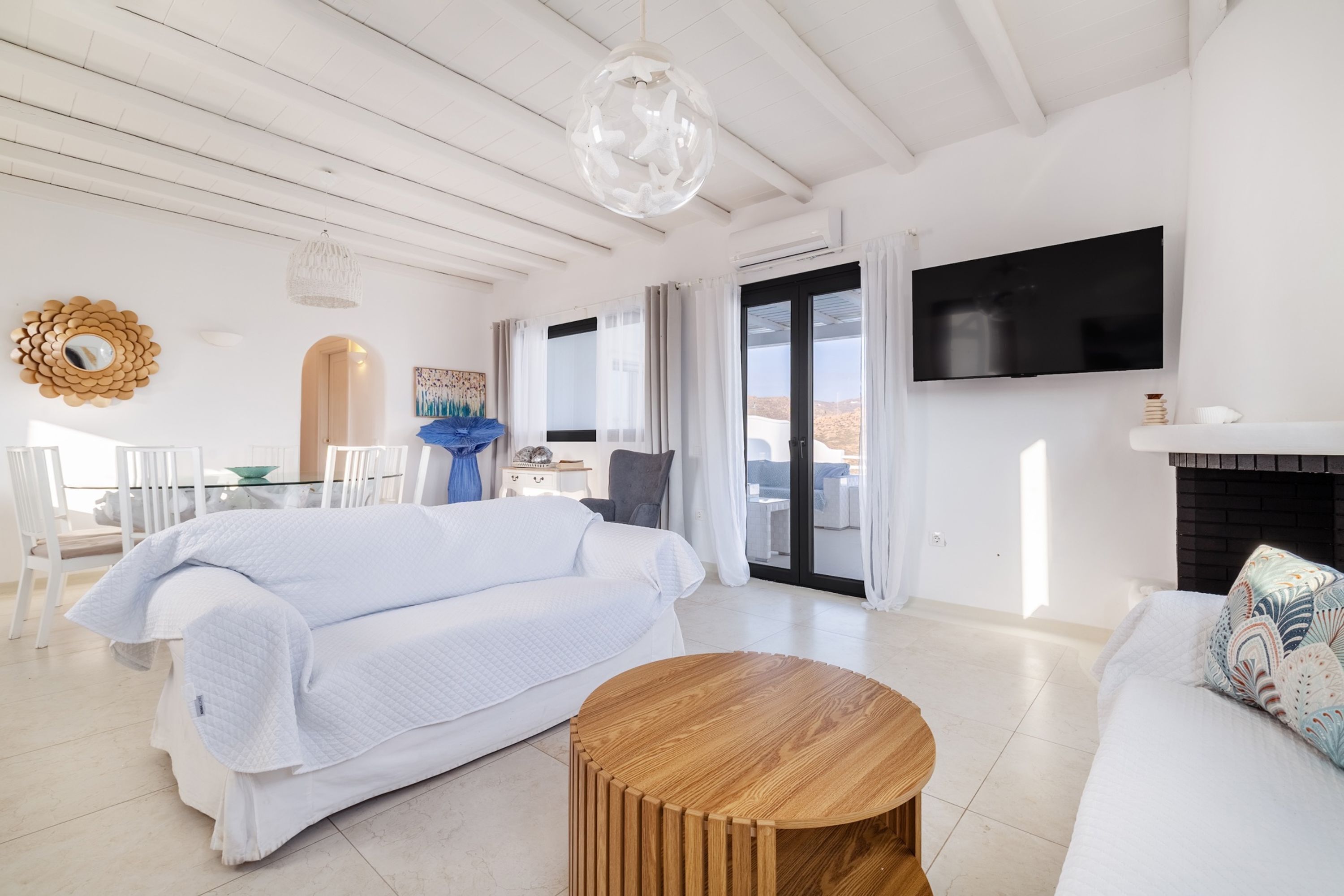 A spacious living room with a white sofa, a wooden coffee table, and a TV mounted on the wall.