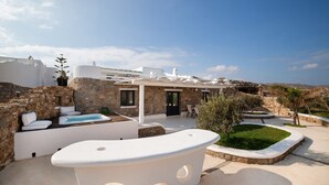 Una villa moderna con fachada de piedra, piscina y zona de patio con mobiliario exterior.