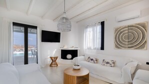Una sala de estar moderna con un sofá blanco, una mesa de centro redonda de madera y un ventanal con vistas a una piscina y edificios.