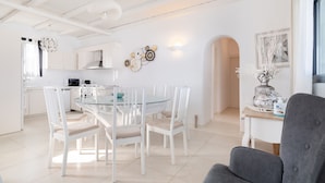 Una cocina moderna con armarios blancos, una mesa de comedor de vidrio y un sillón gris.