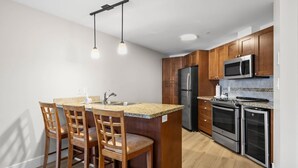 A kitchen with wooden cabinets, stainless steel appliances, a granite countertop, and pendant lighting. - Lakefront Resort Condo with Pool (West Kelowna)