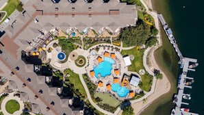 An aerial view of a resort with a central pool area, multiple guest rooms, and a dock with boats. - Lakefront Resort Condo with Pool (West Kelowna)