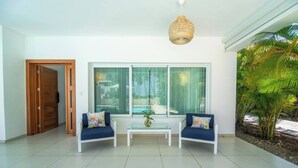 A modern living room with a large window, two blue sofas, a glass coffee table, and a hanging light fixture. - Lux Villa Playa Bonita (Las Terrenas)