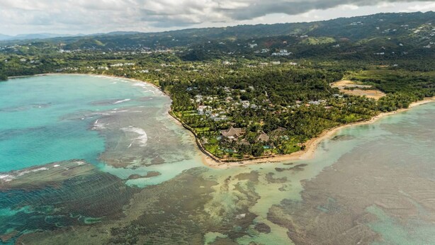 An aerial view of a coastal resort with a beach, dense vegetation, and scattered buildings. - Lux Villa Playa Bonita (Las Terrenas)