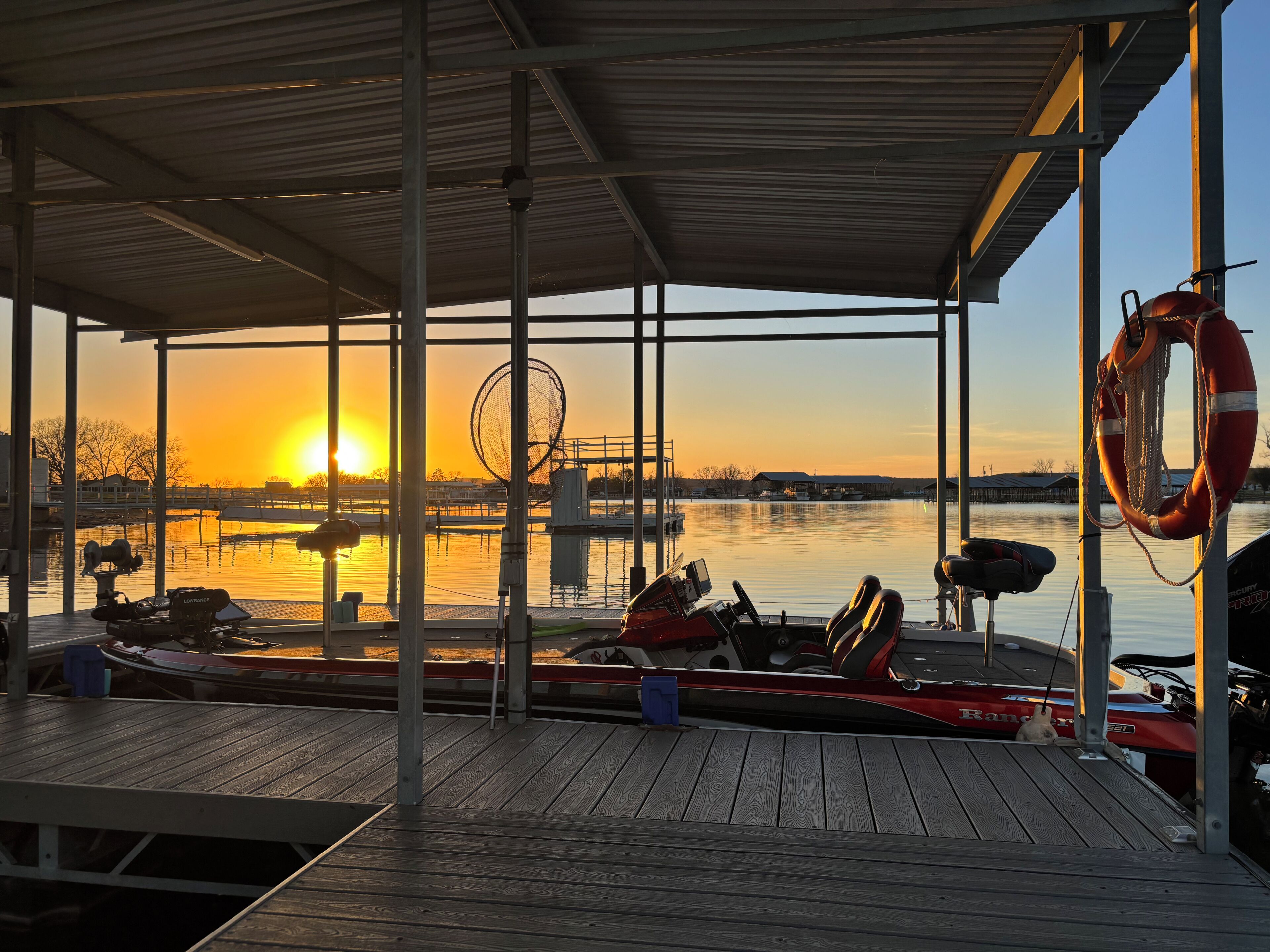 Ein steg mit Booten, einem Rettungsring und Blick auf einen Sonnenuntergang.
