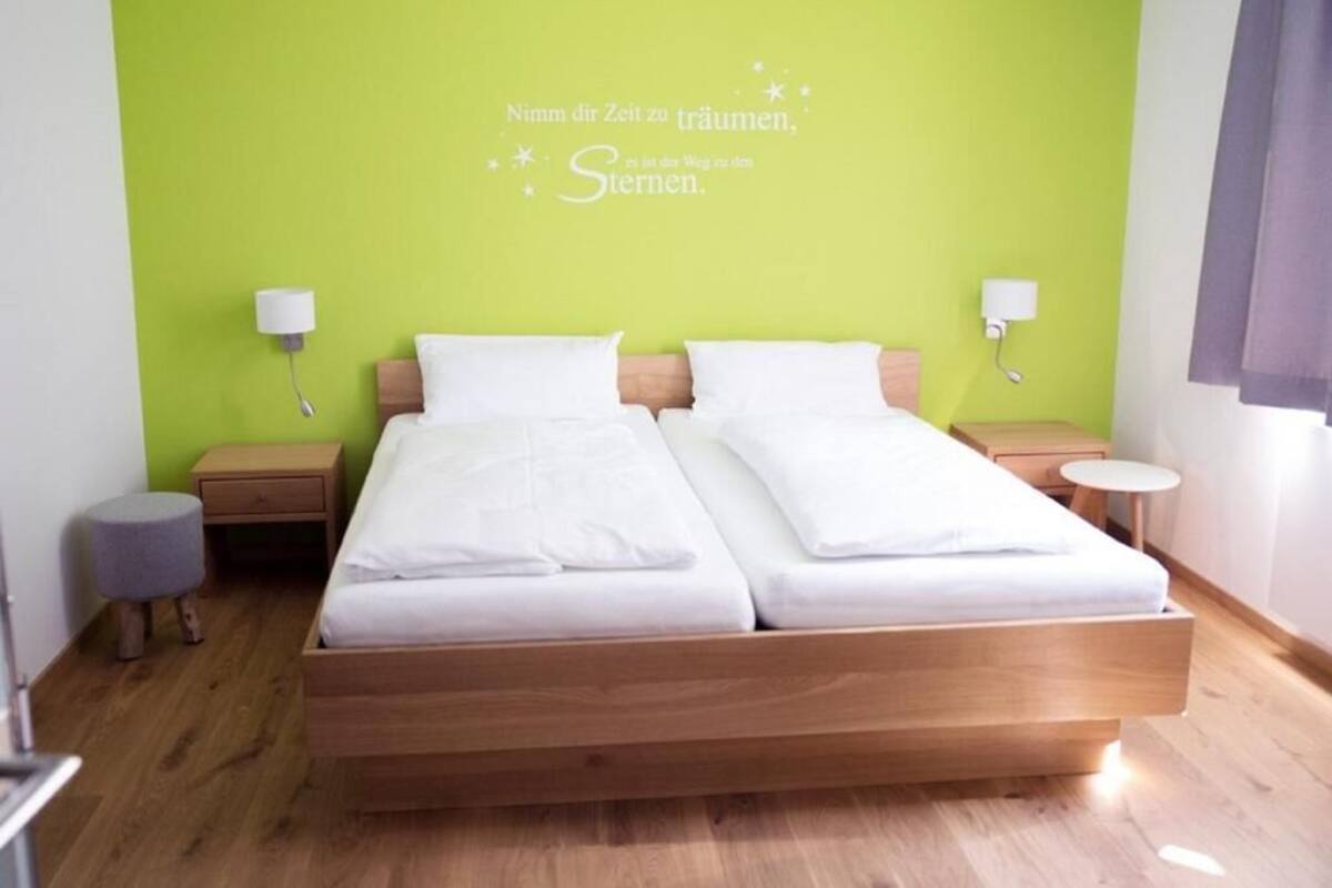 Cama doble con ropa blanca en una habitación con una pared de acento verde.